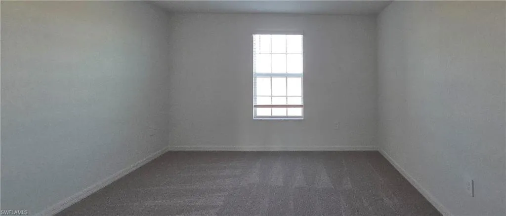 Empty room featuring dark colored carpet and baseboards
