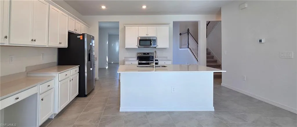 Kitchen with white cabinets, a kitchen island with sink, appliances with stainless steel finishes, light stone counters, and recessed lighting