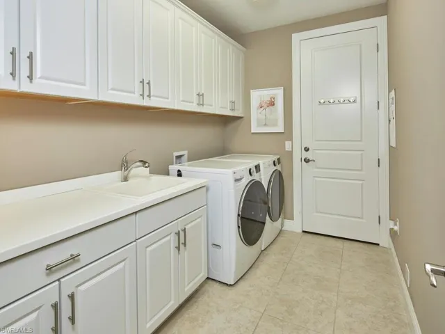 Laundry room featuring sink, light tile patterned floors, washing machine and dryer, and cabinets