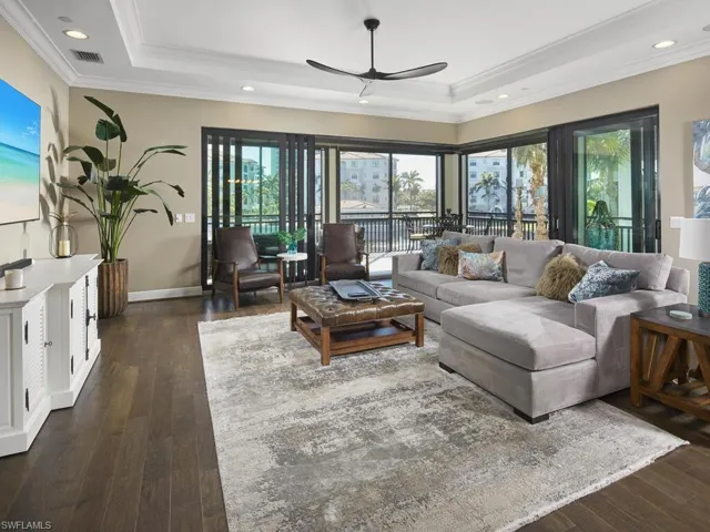 Living room featuring ceiling fan, ornamental molding, a tray ceiling, and dark hardwood / wood-style flooring