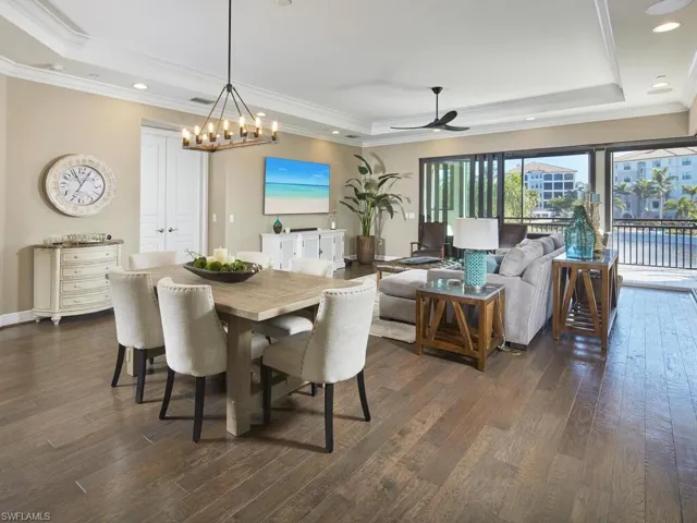 Dining space featuring dark wood-type flooring, crown molding, a raised ceiling, and ceiling fan with notable chandelier