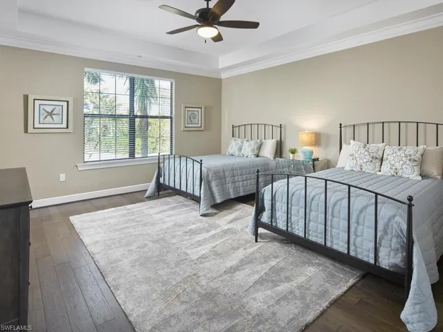Bedroom featuring dark hardwood / wood-style floors, ceiling fan, ornamental molding, and a tray ceiling
