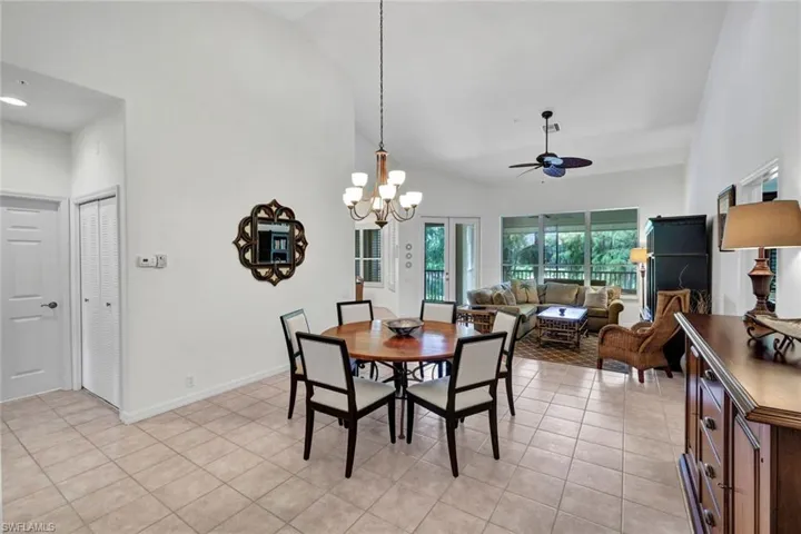 Dining room with light tile patterned floors, a ceiling fan, high vaulted ceiling, and a chandelier