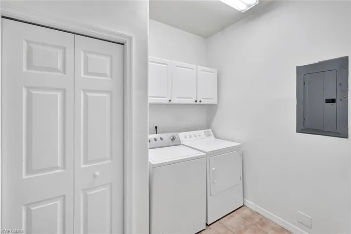 Laundry room with electric panel, cabinet space, separate washer and dryer, and light tile patterned floors