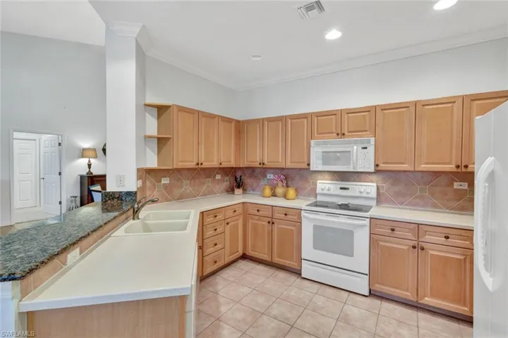 Kitchen featuring white appliances, crown molding, tasteful backsplash, light tile patterned floors, and a peninsula