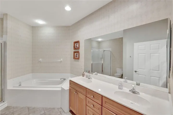 Full bathroom featuring wallpapered walls, a bath, a stall shower, light tile patterned flooring, and double vanity