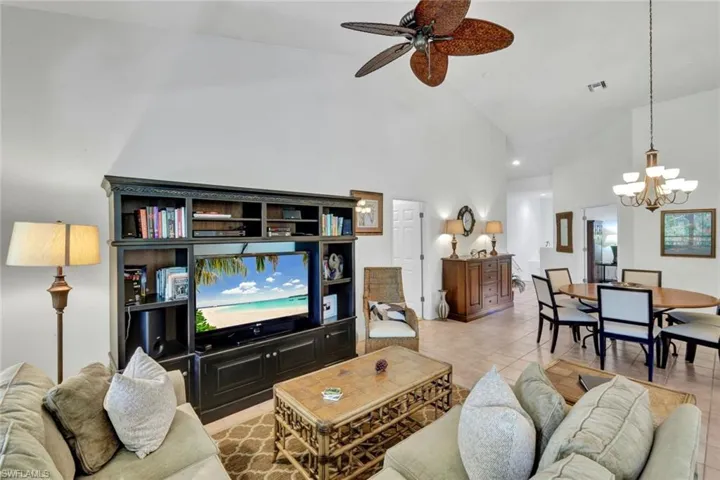 Living area with high vaulted ceiling, ceiling fan, light tile patterned floors, and a chandelier