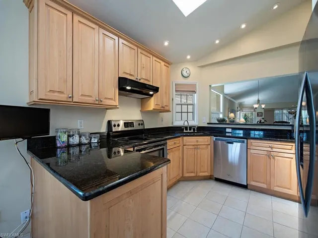 Kitchen with vaulted ceiling, skylight, appliances with stainless steel finishes, kitchen peninsula, and dark stone counters