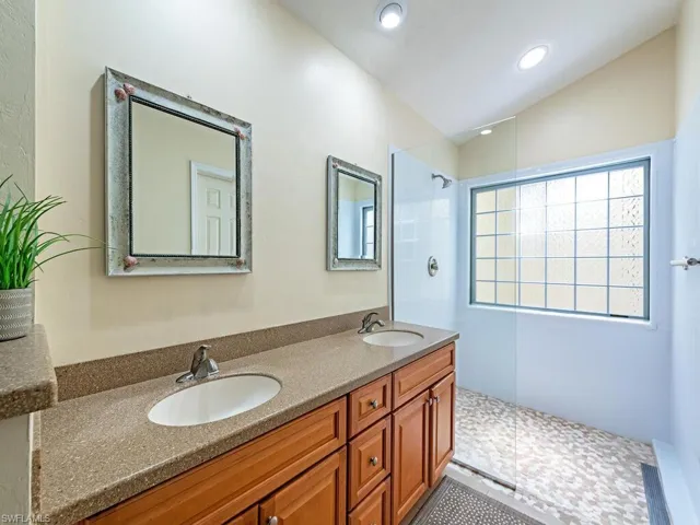 Bathroom featuring double vanity, vaulted ceiling, walk-in shower, and tile floors