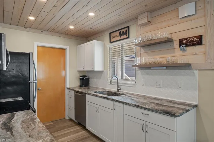 Kitchen with stainless steel appliances, backsplash, wood ceiling, white cabinets, and a sink