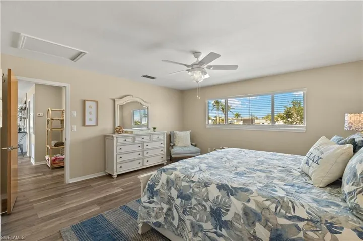 Bedroom with wood finished floors, visible vents, a ceiling fan, baseboards, and attic access
