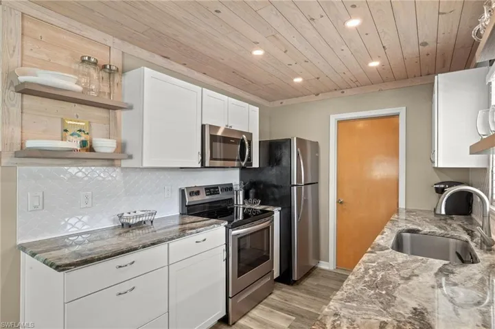Kitchen featuring dark stone countertops, decorative backsplash, stainless steel appliances, and a sink
