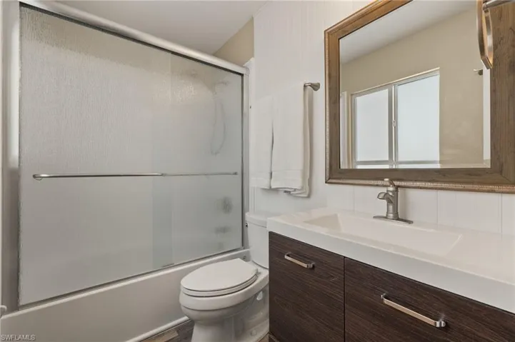 Bathroom with shower / bath combination with glass door, vanity, and toilet