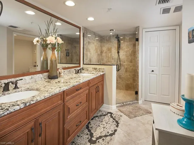 Renovated primary en suite with walk-in shower, wood cabinetry, dual sinks and granite countertops.