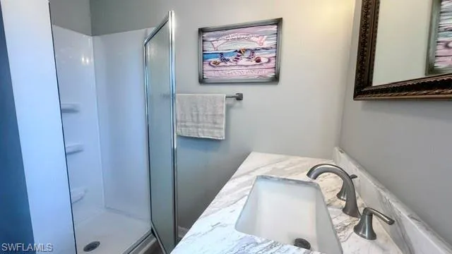 Bathroom featuring a white shower stall with a frosted glass door, a vanity with a light-colored countertop, an undermount sink, and a brushed nickel faucet