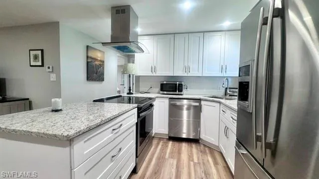 Modern kitchen featuring white shaker cabinetry, stainless steel appliances, speckled stone countertops, and wood-finish flooring