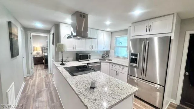 Modern kitchen featuring a central island with a built-in cooktop, white shaker cabinetry, stainless steel appliances, and granite countertops