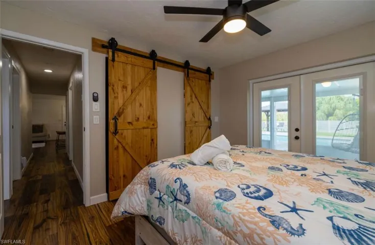 Bedroom with ceiling fan, a barn door, access to exterior, dark wood-type flooring, and french doors