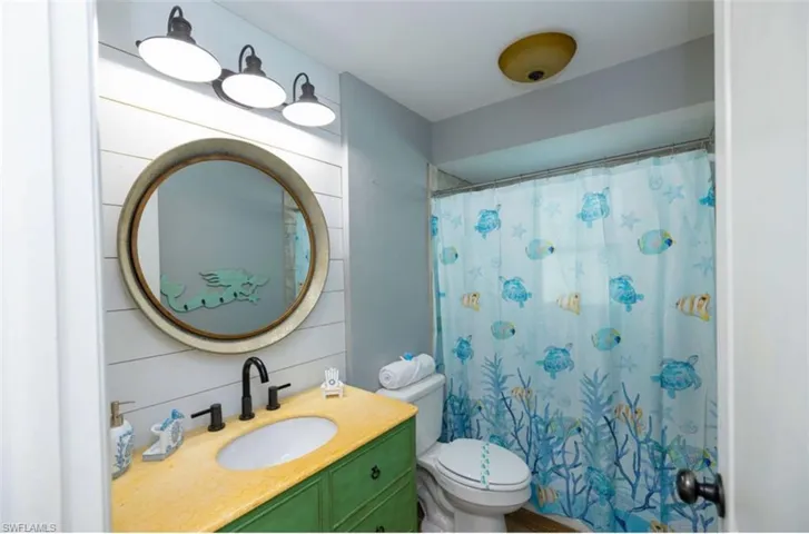 Bathroom featuring toilet, vanity, wood walls, and a shower with curtain