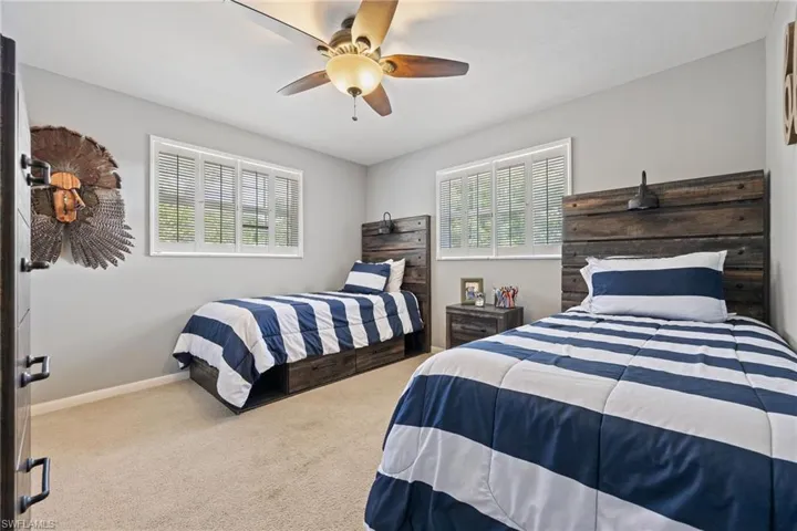 Carpeted bedroom with ceiling fan, baseboards, and multiple windows