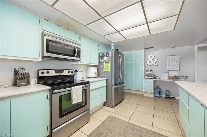 Kitchen with stainless steel appliances, backsplash, light countertops, blue cabinetry, and light tile patterned floors
