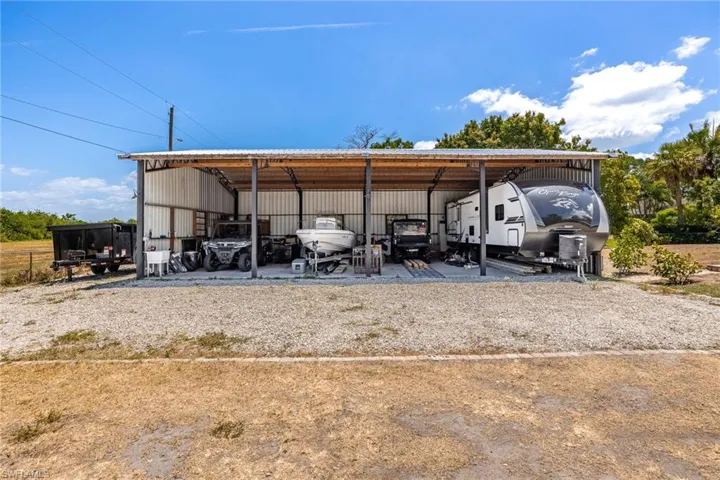 View of parking / parking lot featuring a detached carport, a pole building, and gravel driveway