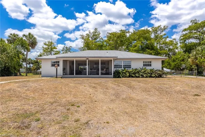 Rear view of property featuring metal roof, a sunroom, fence, and a lawn
