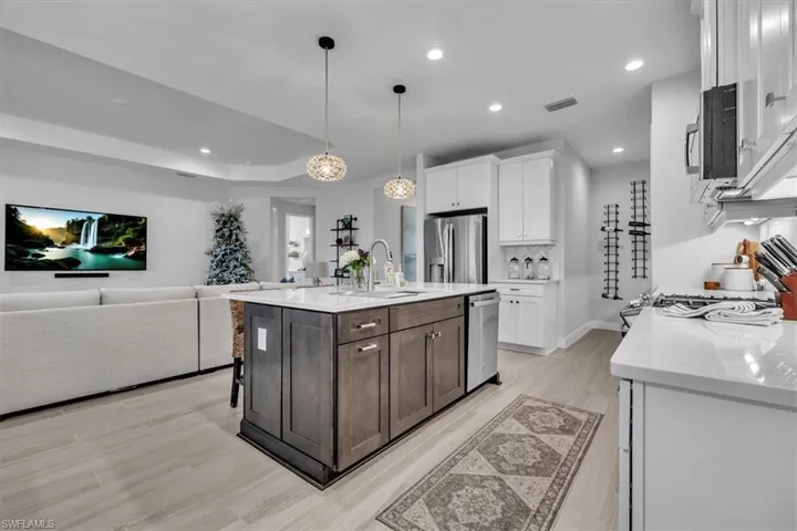 Kitchen featuring white cabinetry, light stone countertops, a kitchen island with sink, decorative light fixtures, and open floor plan