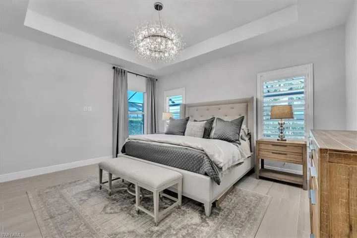 Bedroom featuring a tray ceiling, a chandelier, and light wood-style floors