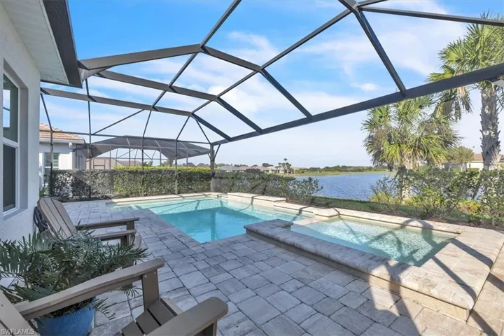 View of pool featuring a sunroom, glass enclosure, a water view, a patio area, and a pool with connected hot tub