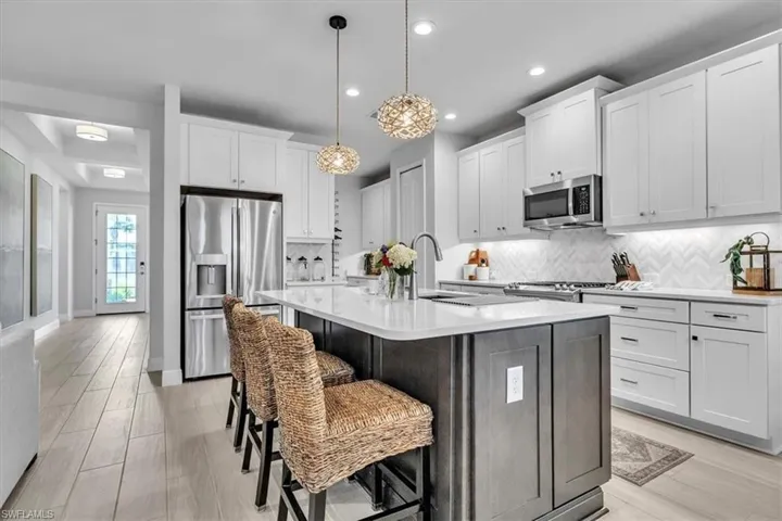 Kitchen featuring appliances with stainless steel finishes, decorative light fixtures, white cabinetry, a kitchen island with sink, and recessed lighting