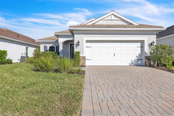 View of front of property featuring stucco siding, decorative driveway, a front lawn, and stone siding