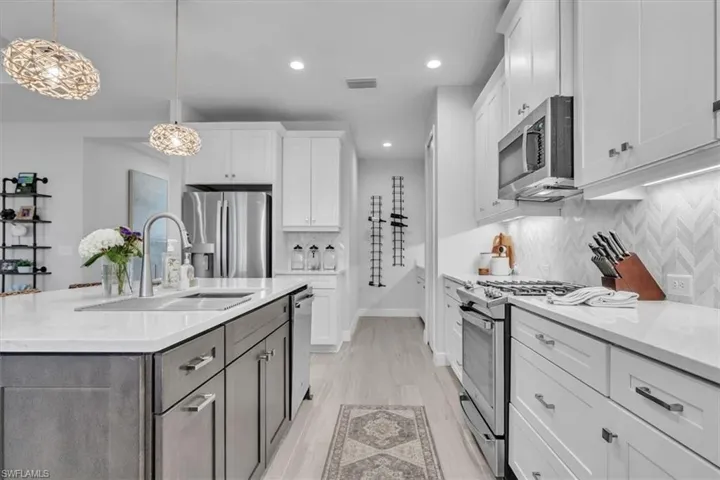 Kitchen featuring decorative light fixtures, white cabinetry, light stone counters, backsplash, and recessed lighting