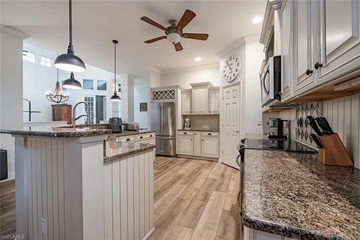 Kitchen featuring ornamental molding, tasteful backsplash, pendant lighting, stone counters, and light wood-style flooring
