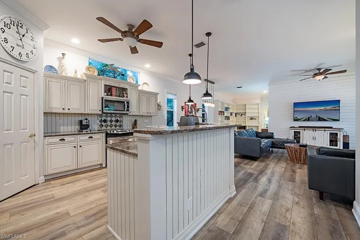 Kitchen with ceiling fan, pendant lighting, stone counters, ornamental molding, and stainless steel appliances.