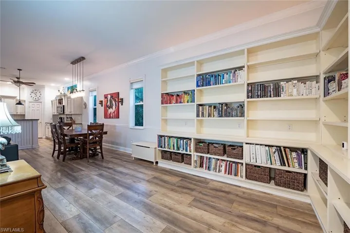 Sitting room off living area with built in bookshelves, ceiling fan, and light wood-type flooring