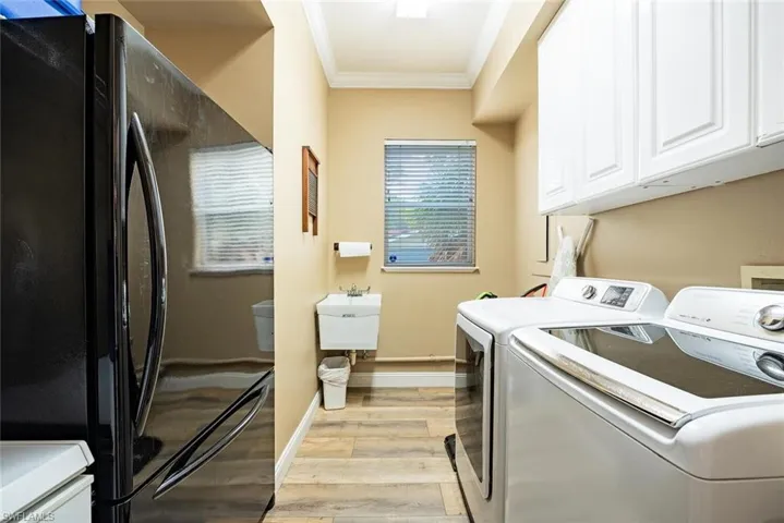 Laundry room featuring crown molding, light wood finished floors, washing machine and clothes dryer, and cabinet space