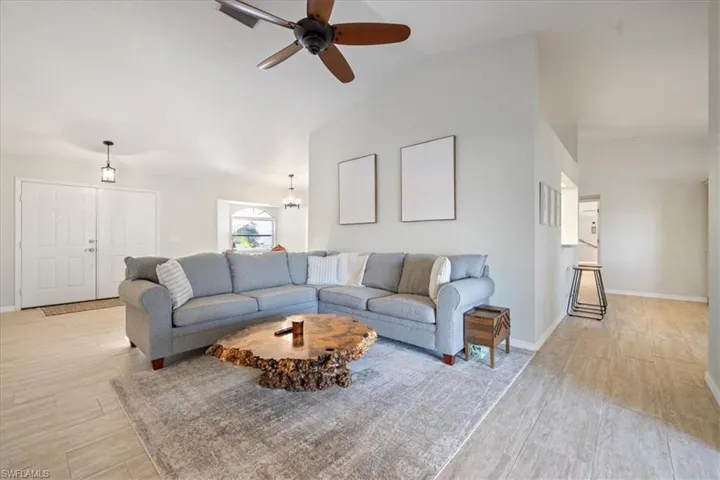 Living room featuring high vaulted ceiling, ceiling fan with notable chandelier, and light hardwood / wood-style floors