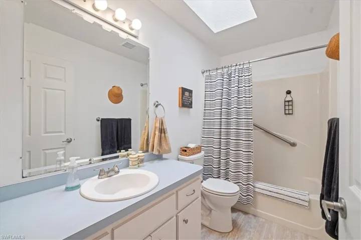 Full bathroom with hardwood / wood-style flooring, a skylight, vanity, shower / bath combination with curtain, and toilet