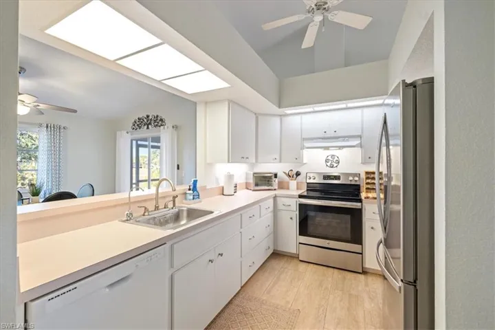 Kitchen featuring sink, kitchen peninsula, stainless steel appliances, vaulted ceiling with skylight, and white cabinets