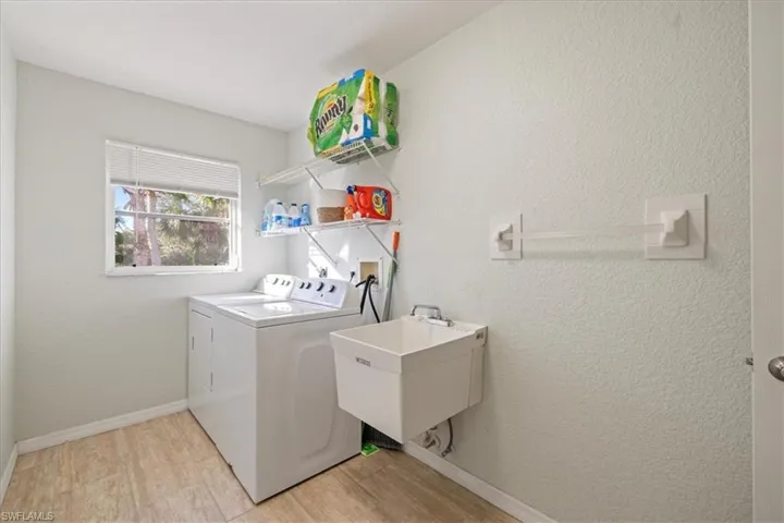 Clothes washing area with light hardwood / wood-style floors, washer and clothes dryer, and sink