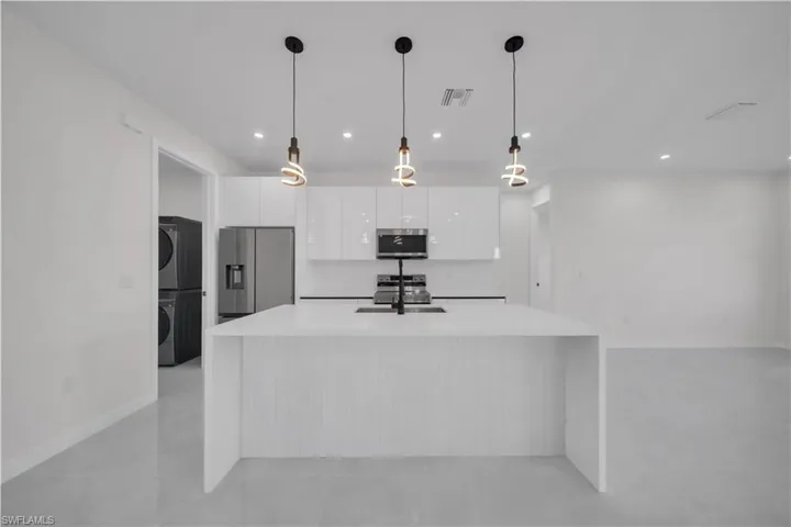 Kitchen with stainless steel appliances, white cabinets, decorative light fixtures, and stacked washer and clothes dryer