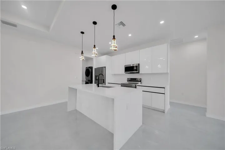 Kitchen featuring white cabinetry, stainless steel appliances, stacked washer and clothes dryer, a center island with sink, and light stone countertops