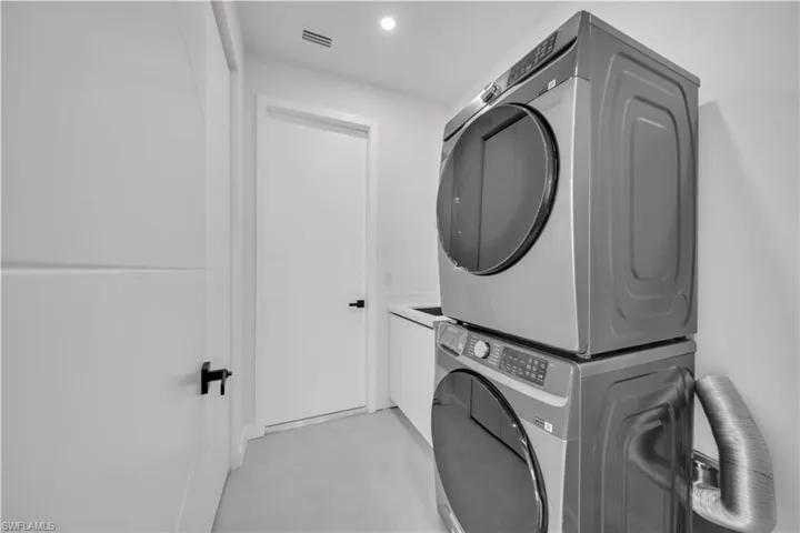 Laundry area featuring stacked washing machine and dryer, finished concrete flooring, cabinet space, and recessed lighting