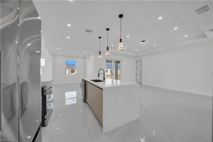 Kitchen with stainless steel appliances, a kitchen island with sink, open floor plan, concrete flooring, and light stone countertops