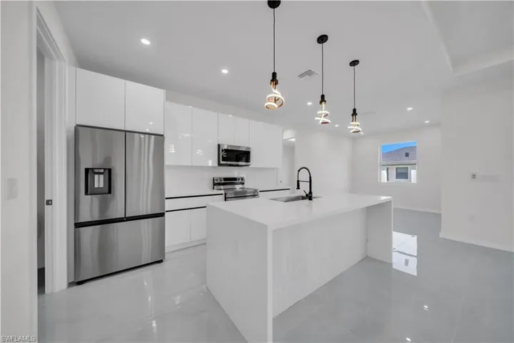Kitchen featuring stainless steel appliances, white cabinets, pendant lighting, an island with sink, and light stone countertops