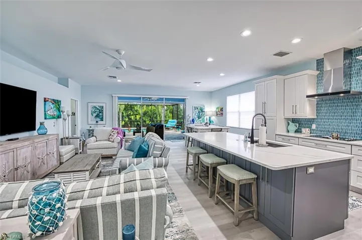 Kitchen with wall chimney exhaust hood, a kitchen island with sink, tasteful backsplash, and white cabinets