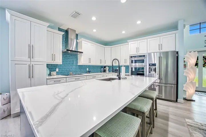 Kitchen featuring appliances with stainless steel finishes, wall chimney exhaust hood, sink, and white cabinets