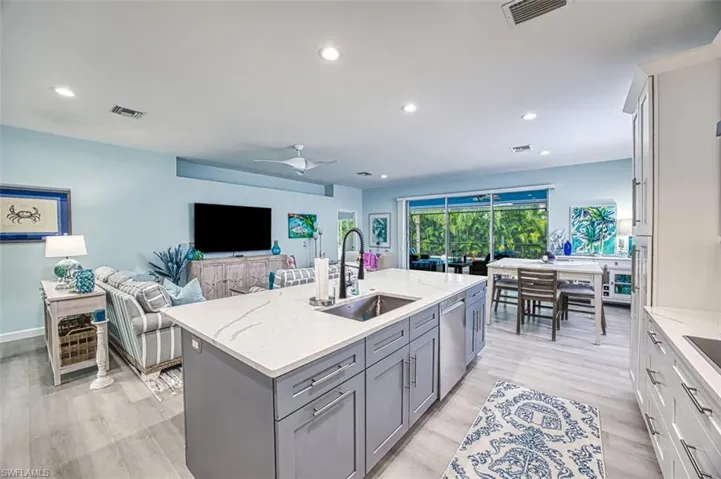 Kitchen featuring dishwasher, light stone countertops, ceiling fan, a center island with sink, and sink