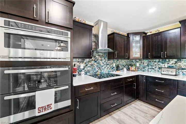 Kitchen featuring build-in stainless steel double oven, build-in stainless micro wave, build-in glass stove top, dark brown solid-wood cabinets, ventilation hood, and light quartz counters